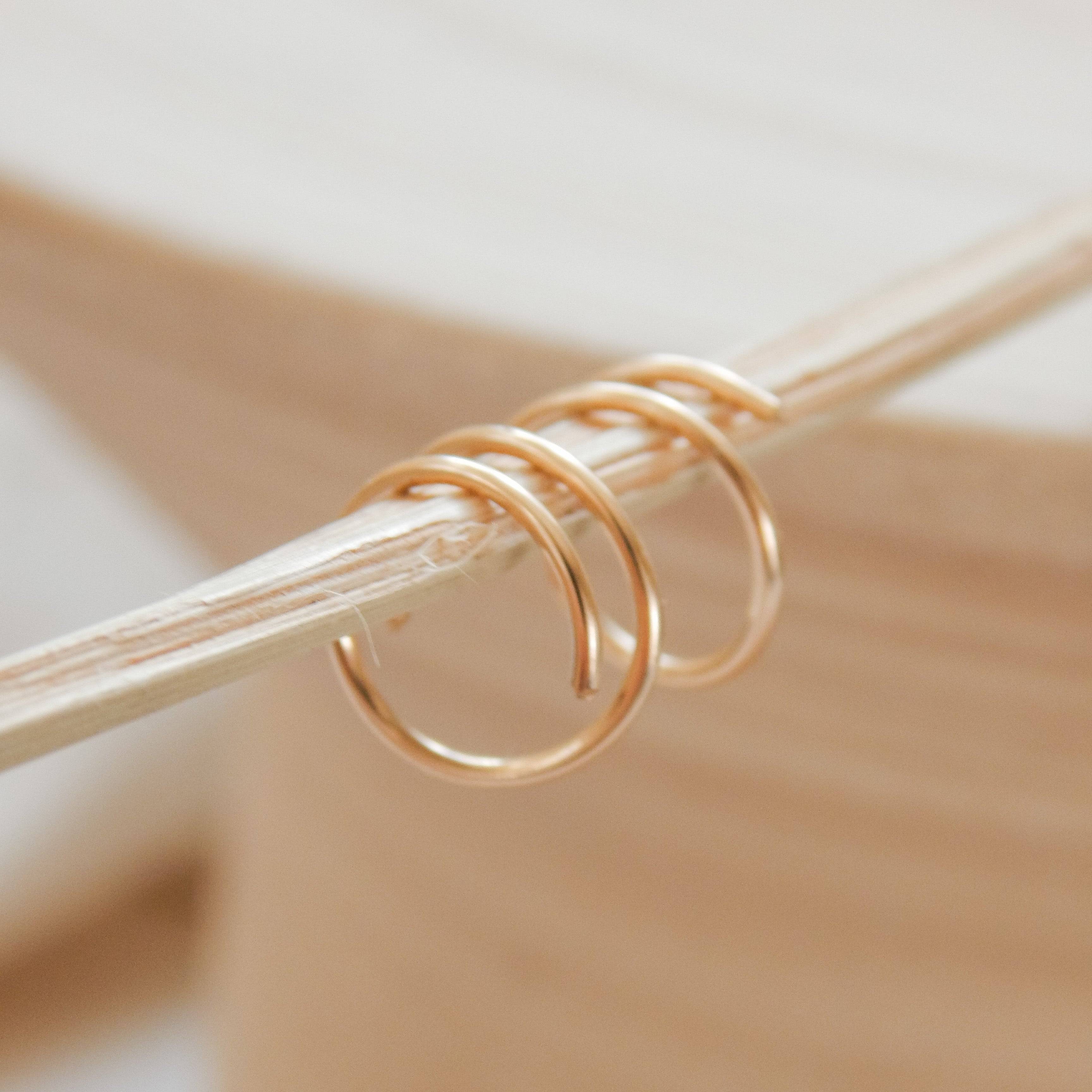 Close-up of Twist-In Double Huggie Hoop Earrings in gold, delicately wrapped around a neutral-toned prop for Barberry & Lace Jewelry.