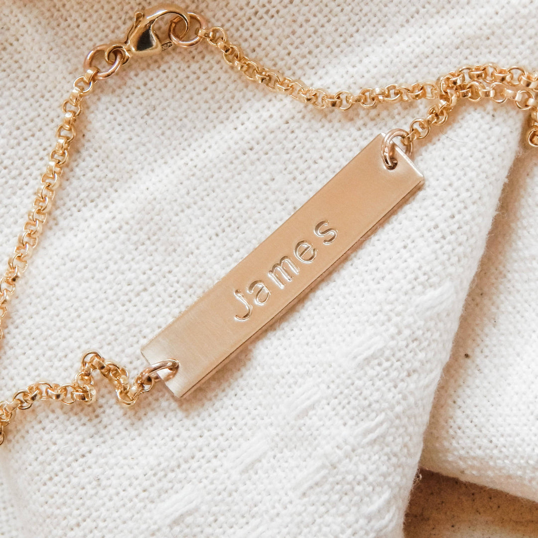 Personalized Bar Bracelet by Barberry & Lace Jewelry featuring a gold bar engraved with the name 'James', hypoallergenic and tarnish-resistant.