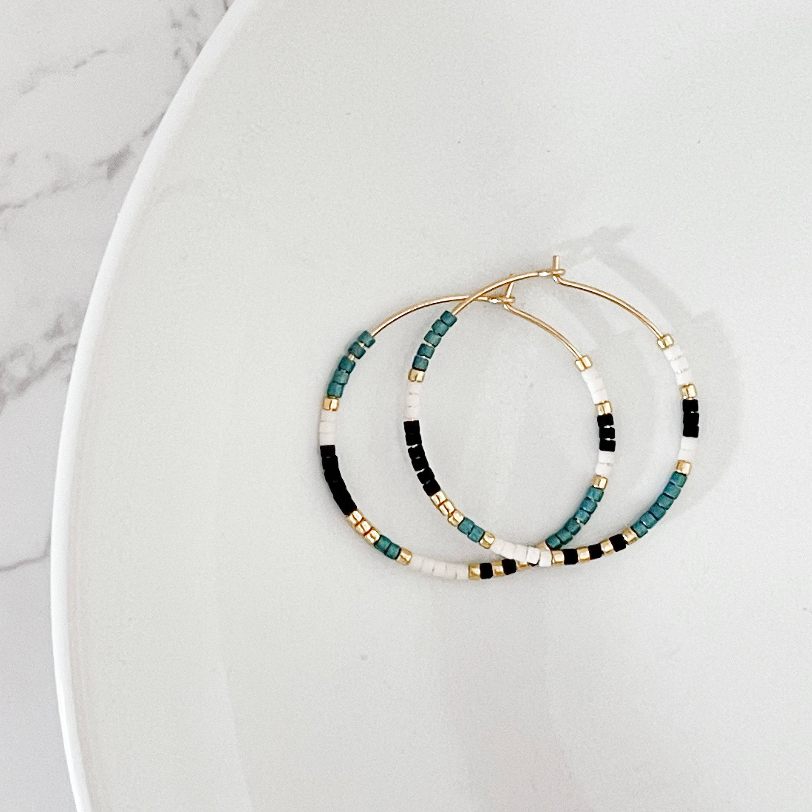 Bold colorway of Summer Edition - Beaded Hoop Earrings with black, teal, white, and gold seed beads on gold hoops, laid flat on a white dish.