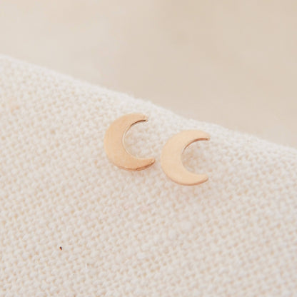 Crescent Moon Stud Earrings | Barberry & Lace Jewelry displayed on soft fabric, featuring dainty gold crescent moons perfect for hypoallergenic wear.