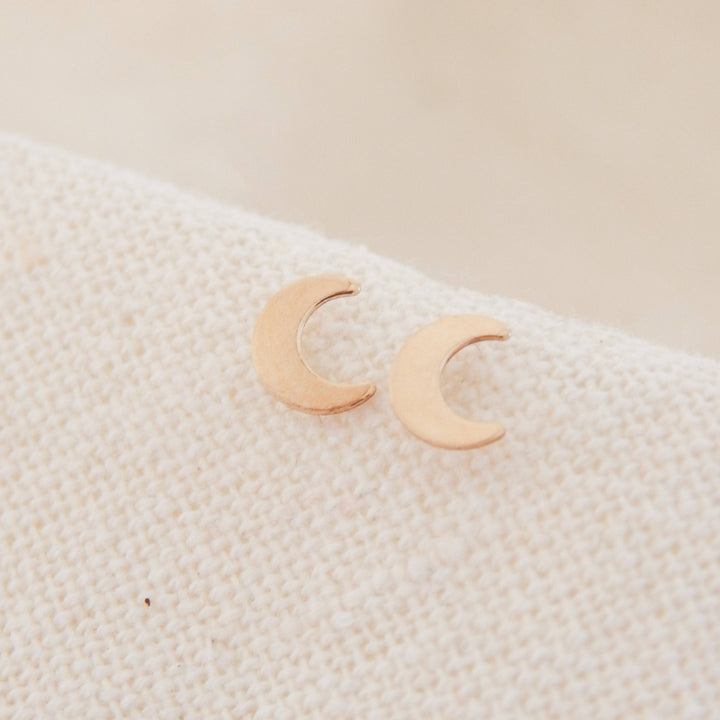 Crescent Moon Stud Earrings | Barberry & Lace Jewelry displayed on soft fabric, featuring dainty gold crescent moons perfect for hypoallergenic wear.